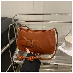 Detail of caramel brown leather shoulder bag featuring decorative metal buckle and knotted strap