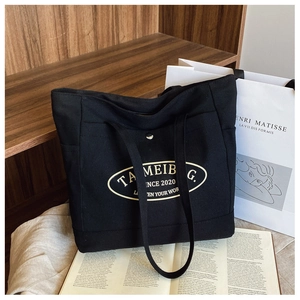 Close-up of black canvas tote bag with gold logo on a wooden shelf with art books