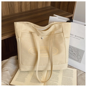 Detail of beige canvas tote bag showing the yellow logo and front pocket with snap button