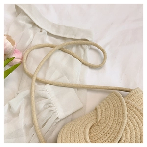 Dettaglio borsa a secchiello intrecciata beige con tracolla su tessuto bianco e tulipani