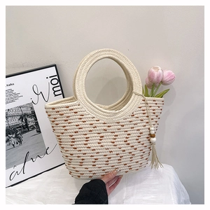 Detail of woven straw tote bag featuring brown polka dots and wooden bead tassel