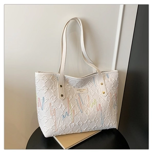 Détail d'un sac cabas blanc matelassé avec broderies ondulées colorées et plaque de logo