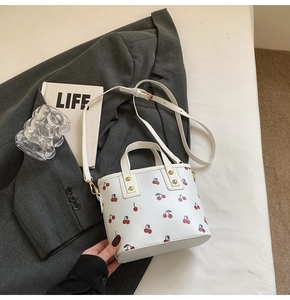 Close-up of stylish cherry print white tote bag with golden rivets on a grey suit