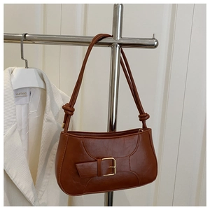 Detail of dark brown leather underarm bag featuring a gold buckle and knotted shoulder strap
