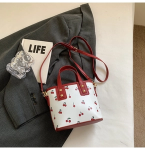 Detail of white bucket bag with cherry print, red leather straps, and gold stud accents