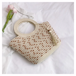 Détail du sac cabas tissé avec textures brunes, poignées circulaires et pompon bohème
