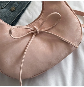 Détail du sac hobo rose avec un nœud décoratif sur une surface en similicuir mat et lisse