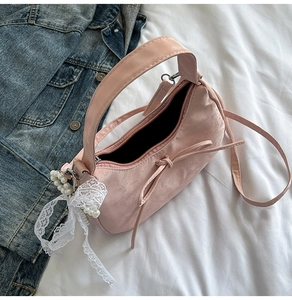 Detailed close-up of pink satin handbag with bow and pearl lace charm on white linen