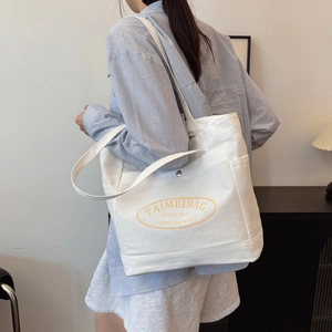 Minimalist white canvas tote bag with orange logo print worn on shoulder for commuting