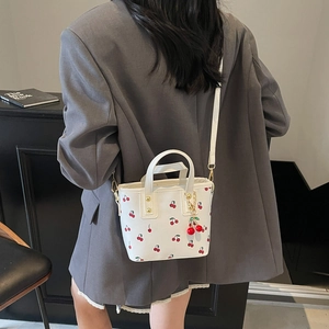 White bucket bag with cherry print and matching pendant worn by model in a suit