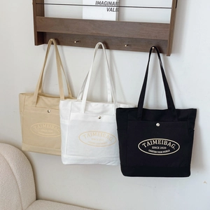 Three minimalist canvas tote bags in beige, white and black hanging on a wooden rack