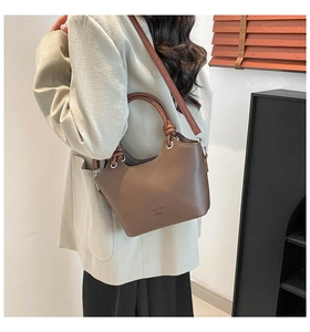 Close-up of brown leather bucket bag featuring unique knotted handle and shoulder strap