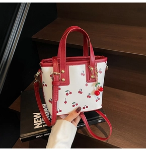 Detailed close-up of a white bucket bag featuring cherry prints and red leather straps