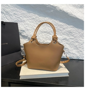 Detail of brown leather bucket bag with knotted handles and fashion logo on white book