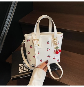 Detail of white leather bucket bag with cherry patterns and a cute 3D cherry charm