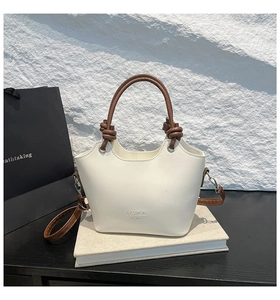 Detail of white bucket bag showing brown handles, knot decor, and fashion logo text