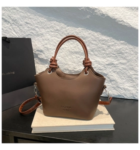 Detail view of brown minimalist bucket bag with knotted handle on white stone background