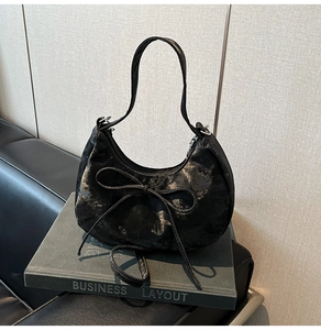 Détail du sac hobo noir avec texture dorée vieillie et nœud sur décor professionnel