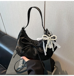 Détail du sac hobo noir avec nœud 3D et breloque en perles sur un livre rétro