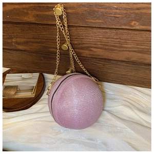 Macro shot of glittery pink spherical clutch bag on white satin with golden chain strap