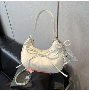 Détail du sac croissant blanc cassé avec nœud délicat, perles et pendentif en dentelle