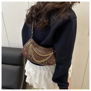 Détail du sac sous l'aisselle à motif crocodile marron foncé avec chaîne dorée et rivets
