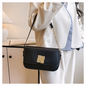 Detail of a black square shoulder bag with a gold geometric lock on an ivory blazer