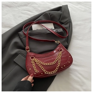 Détail macro du similicuir crocodile bordeaux avec chaînes dorées et clous du sac