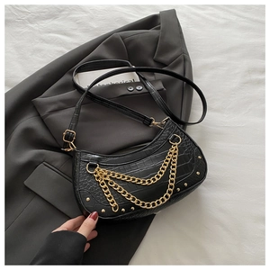 Détail de la texture cuir croco noir avec chaînes dorées superposées et clous métalliques