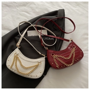 Détail de sacs crème et bordeaux avec motif crocodile et chaînes dorées sur veste noire