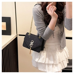 Detail of a black glitter chain bag with gold fringe logo on a model in a gray outfit