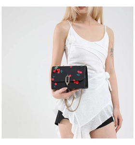 Detail of cherry print on black crossbody bag with gold U-shaped metal lock and chain strap