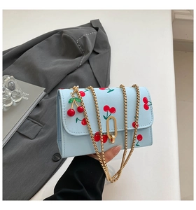 Close-up of blue cherry print handbag featuring a gold U-shaped lock and chain strap