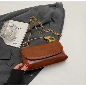 Détail d'un sac à rabat en cuir marron avec une poignée trombone dorée sur un costume