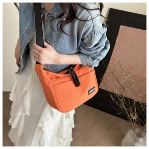 Close-up of orange crescent messenger bag with fashion logo and woven zipper pull detail