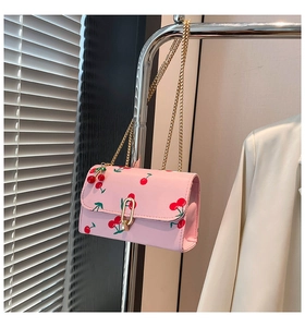 Detail of pink crossbody bag featuring cherry print, metal chain, and cute cherry pendant