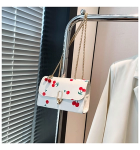 Detail of white cherry print crossbody bag with gold buckle and cute cherry charm