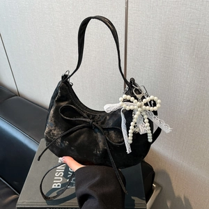 Detail of black crescent handbag featuring velvet fabric and elegant pearl bow pendant