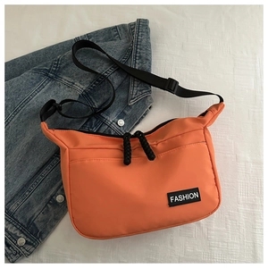Dettaglio borsa a tracolla in nylon arancione con patch su una giacca di jeans blu