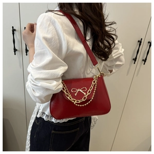 Detailed view of red glossy leather shoulder bag with gold bow clasp and metal chain strap