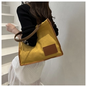 Close-up of bright yellow corduroy tote bag with brown straps and leather logo patch