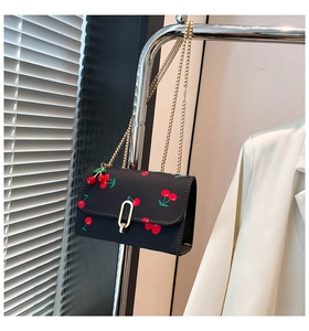 Detail of cherry print on black crossbody bag with gold chain and oval lock