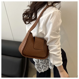 Gros plan du sac bandoulière en similicuir marron tressé porté par un mannequin de profil