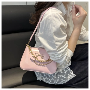 Detail of pink PU leather underarm bag featuring a golden bow buckle and chain strap