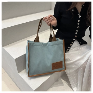 Close-up of light blue canvas tote bag with brown leather handles and brand tag detail
