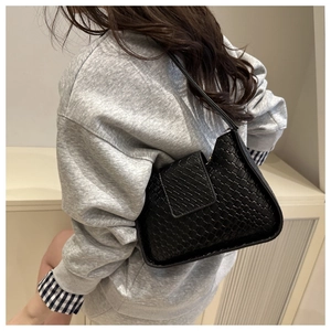 Détail de la texture tressée noire d'un sac porté épaule minimaliste sur un modèle