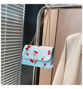 Detail of light blue cherry print crossbody bag with gold chain strap and lock closure