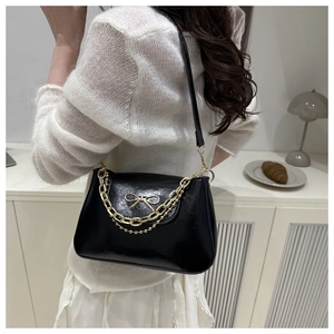 Detail of black glossy baguette bag with gold bow accent and layered chain on a model