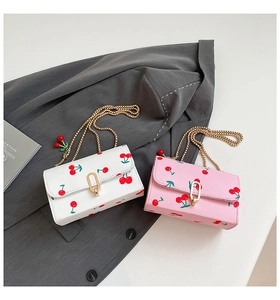 Detail of cherry print flap bags with gold chain straps and cherry pendants on grey fabric