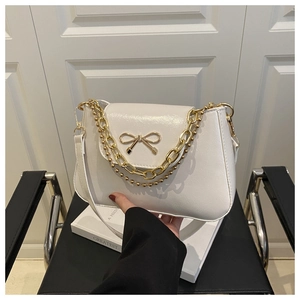 Detail of white PU leather bag with golden bow hardware and chunky metal chain straps